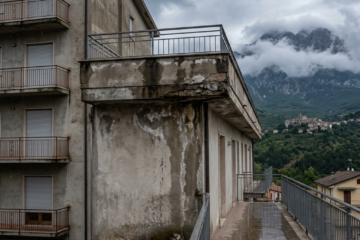 Weathered apartment building and wet walkway overlooking misty mountains and a hillside village